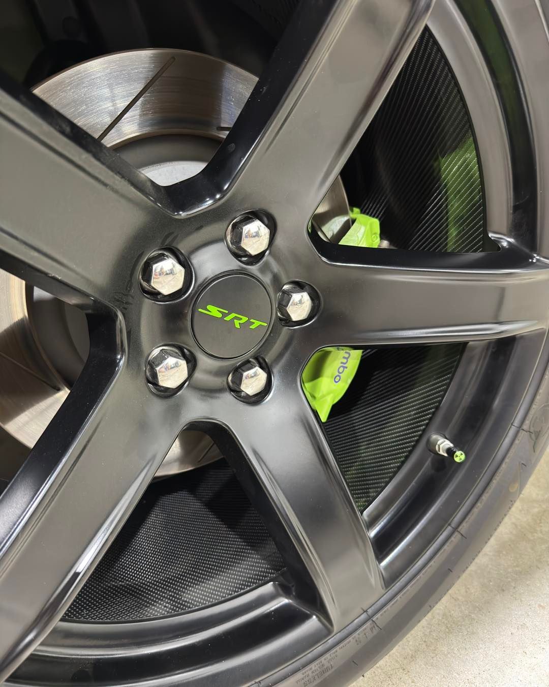 Close-up of a matte black alloy wheel with neon green brake calipers and mesh behind the spokes