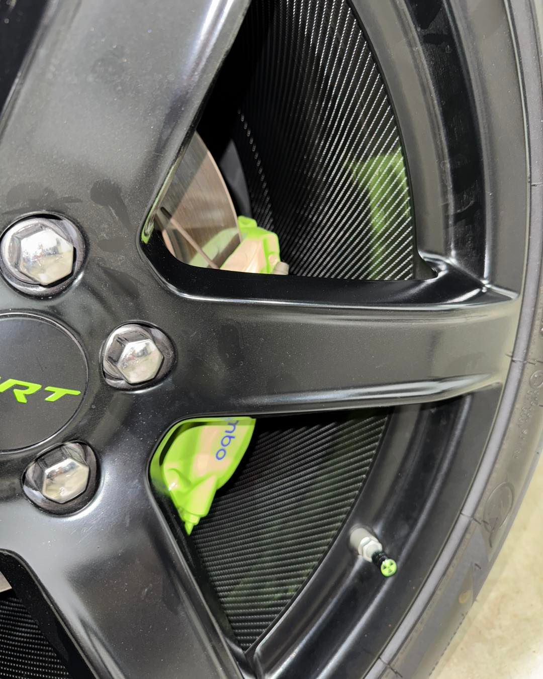 Close-up of a black alloy wheel with lime-green item wedged behind the spokes.