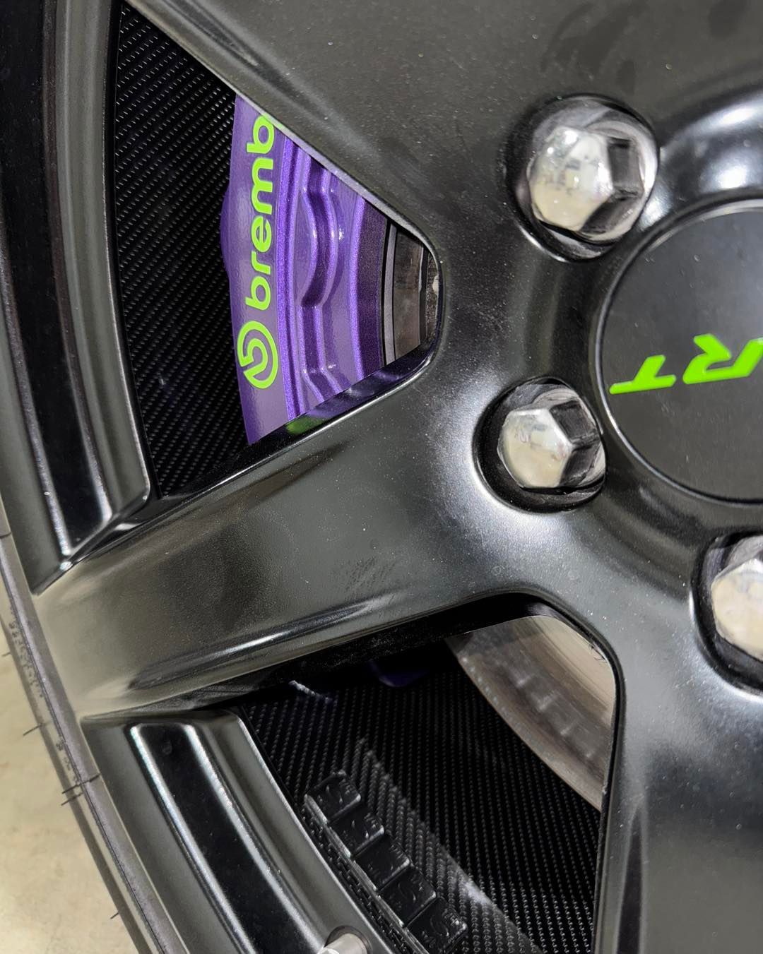 Close-up of a black car wheel with neon green Brembo brake caliper visible through the spokes.