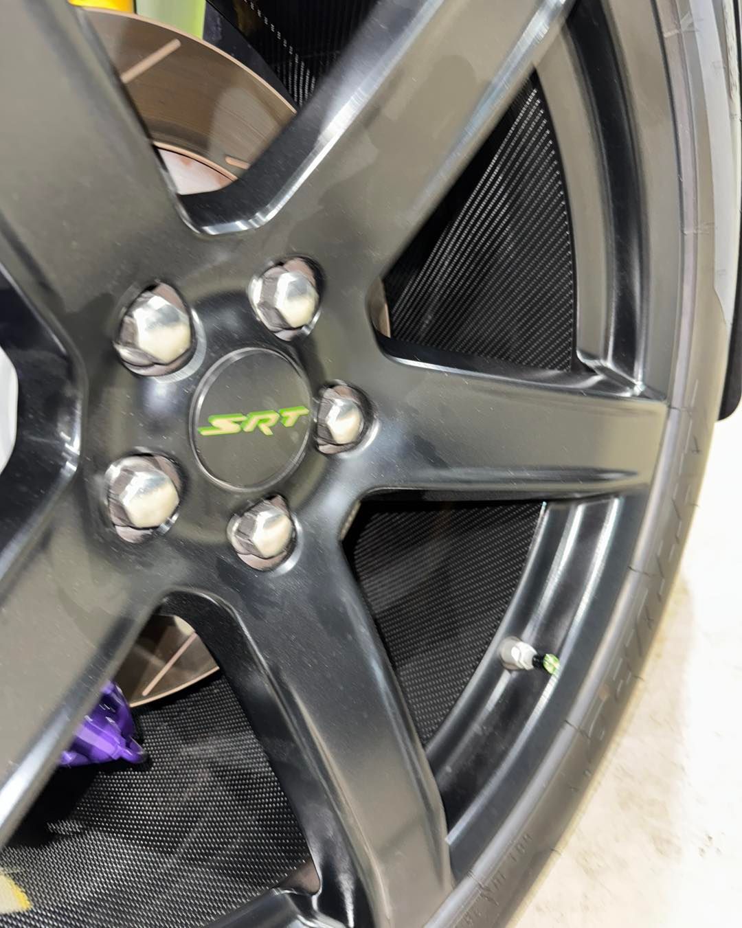 Close-up of a dark gray alloy wheel with five lug nuts and a green center cap.