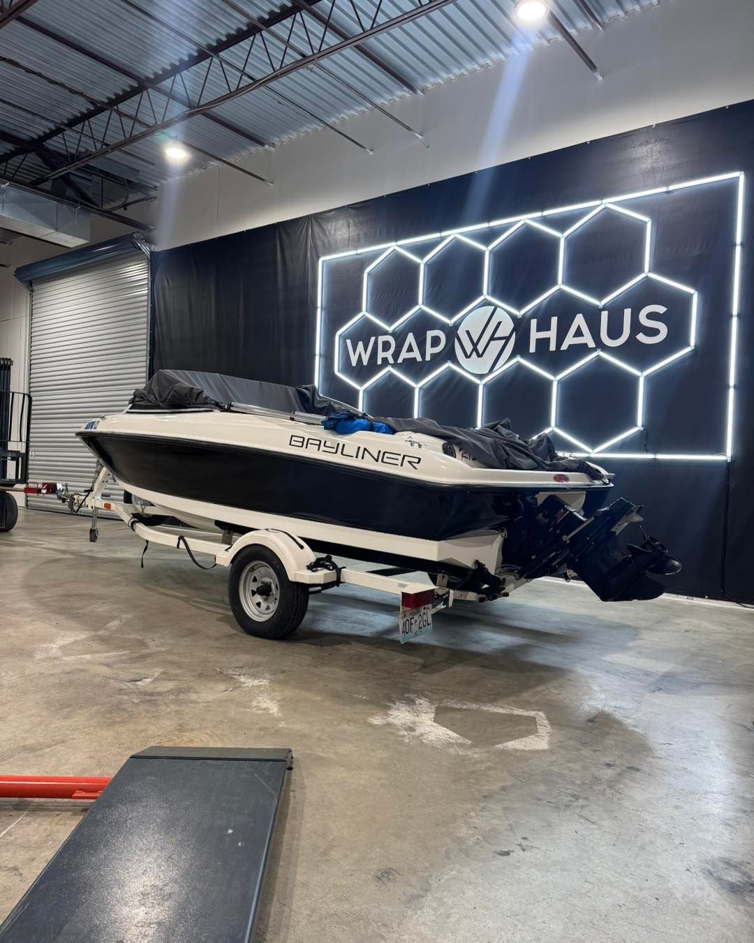 White speedboat on a trailer inside a garage with a glowing “Wrap Haus” sign on the wall