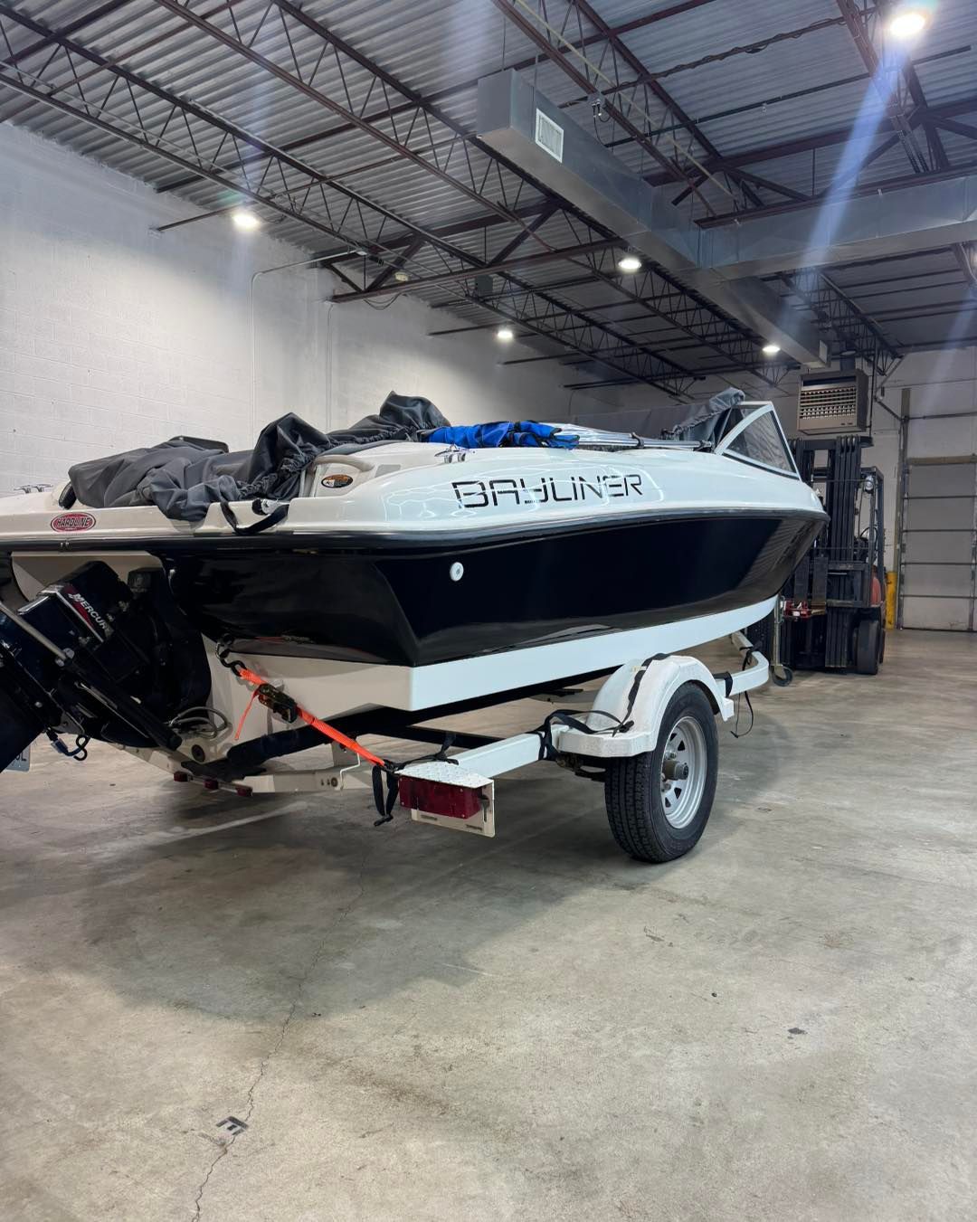 White and black boat on a trailer in a warehouse, with “Bayliner” visible on the hull.