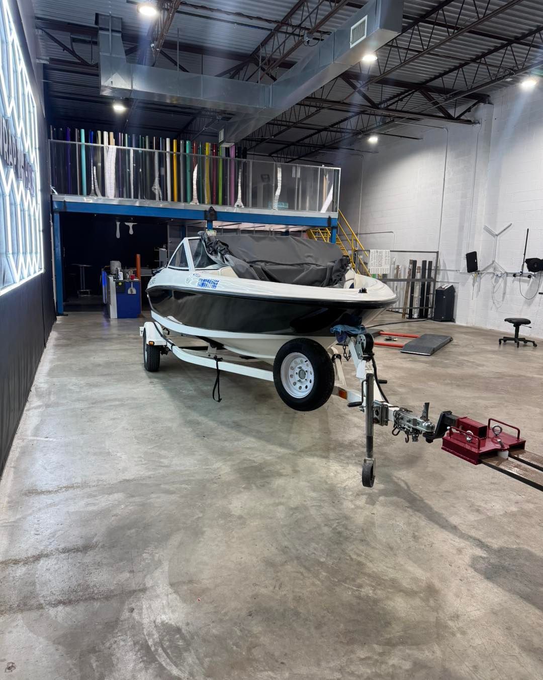 Boat on a trailer in a workshop, with tools and equipment on the concrete floor.
