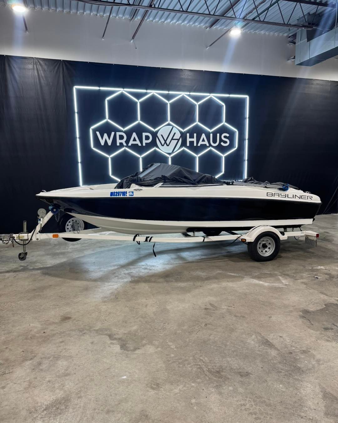 White-and-black jet ski on a trailer inside a garage with a lit WRAP HAUS sign on the wall