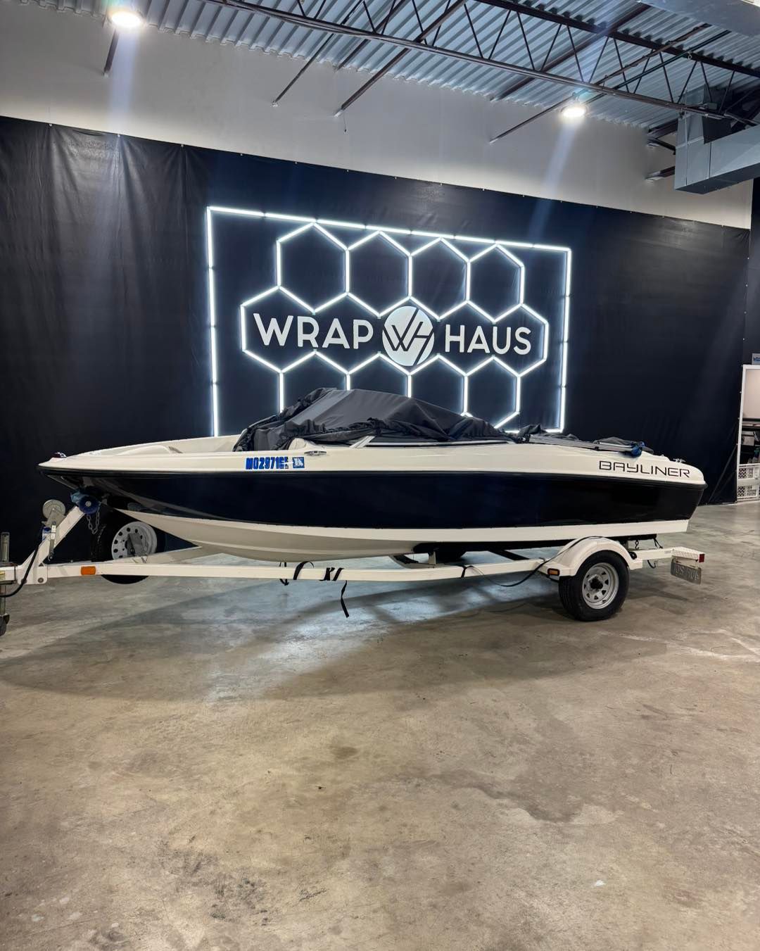 Black-and-white motorboat on a trailer in a showroom with a WRAP HAUS sign
