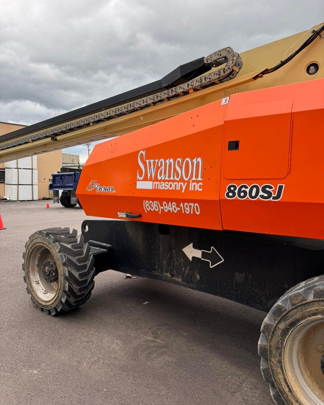 Orange Skyjack 860SJ boom lift parked outdoors, with black wheels and beige boom arm.