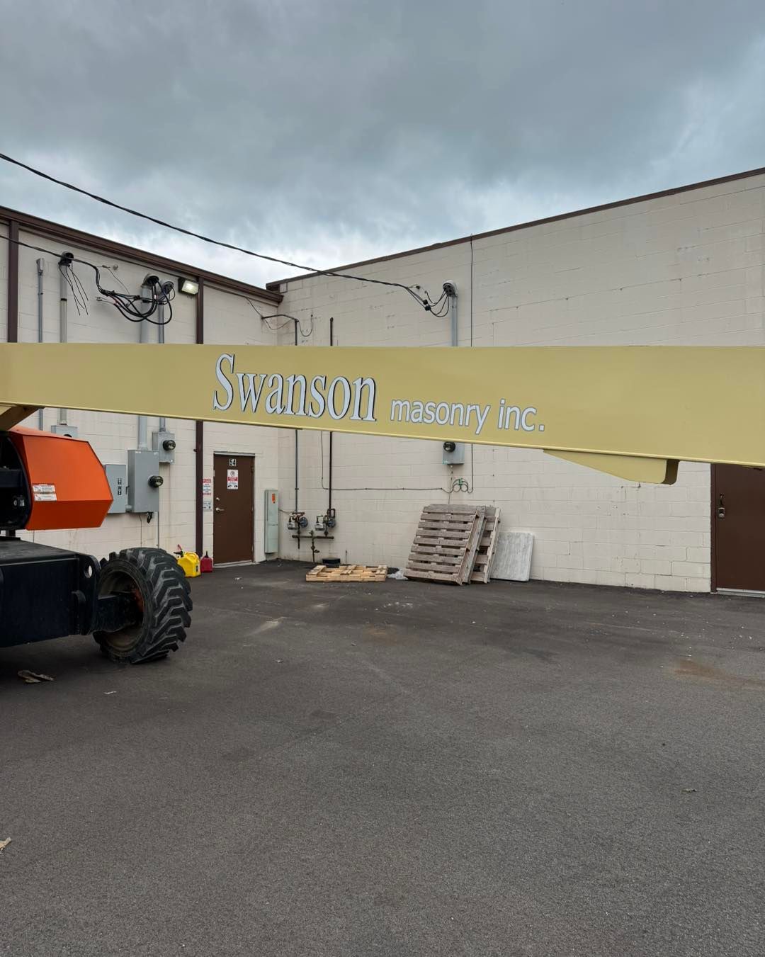Industrial warehouse entrance with a yellow banner, stacked pallets, and a tractor parked outside.