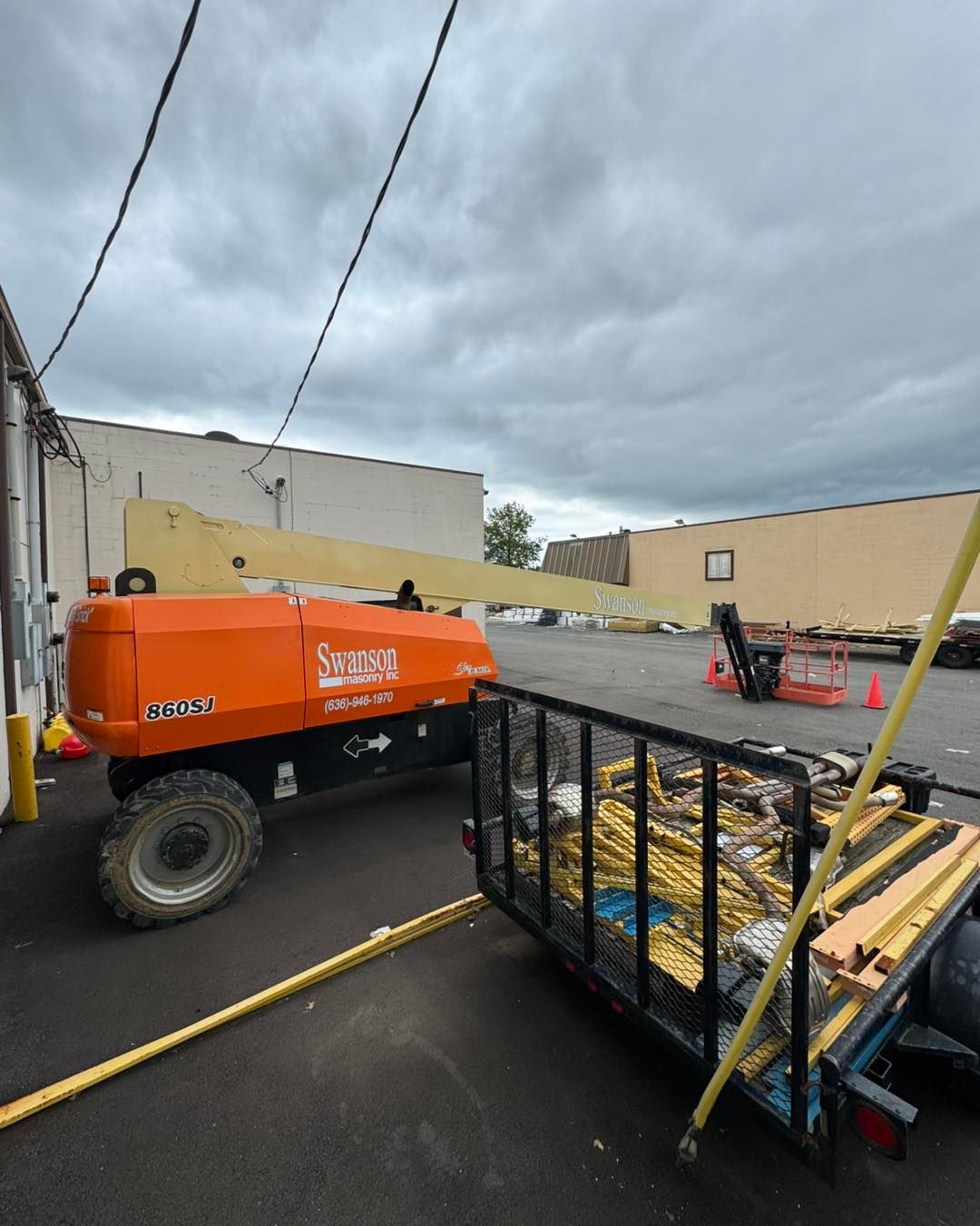 Orange boom lift and pallet rack in a parking lot under cloudy sky