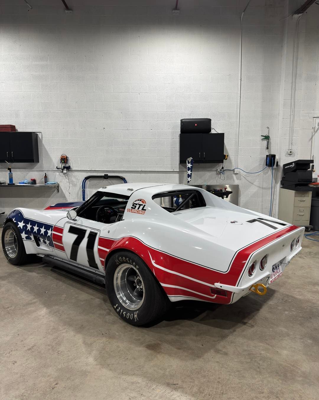 White vintage race car with red and blue stripes parked in a garage, number 71 on the side