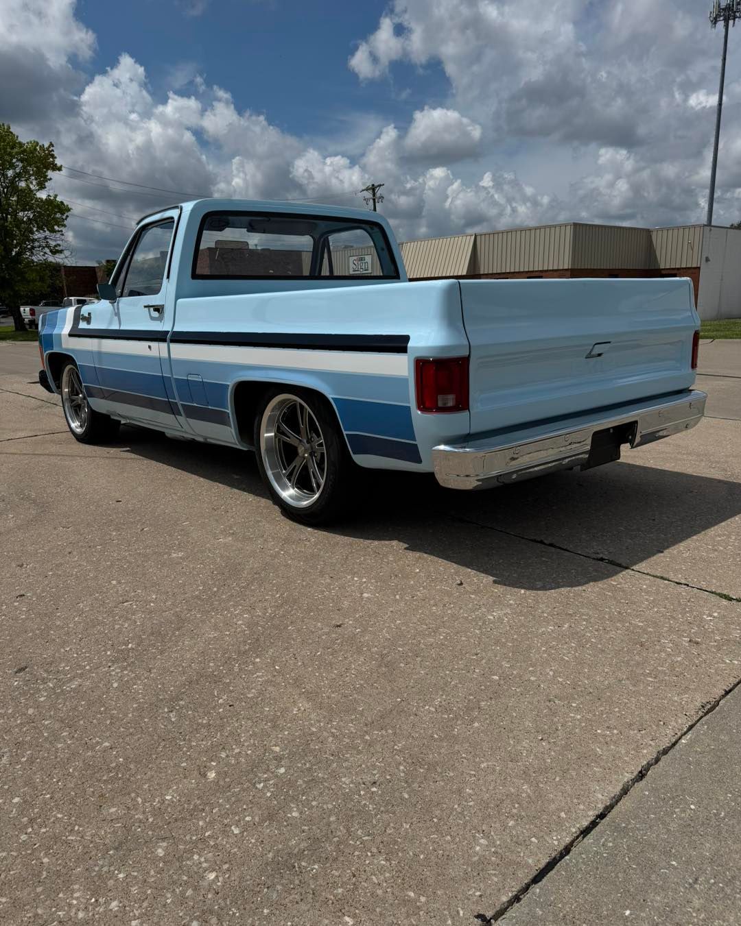 Light blue and white lowered pickup truck parked on a paved lot under cloudy skies.