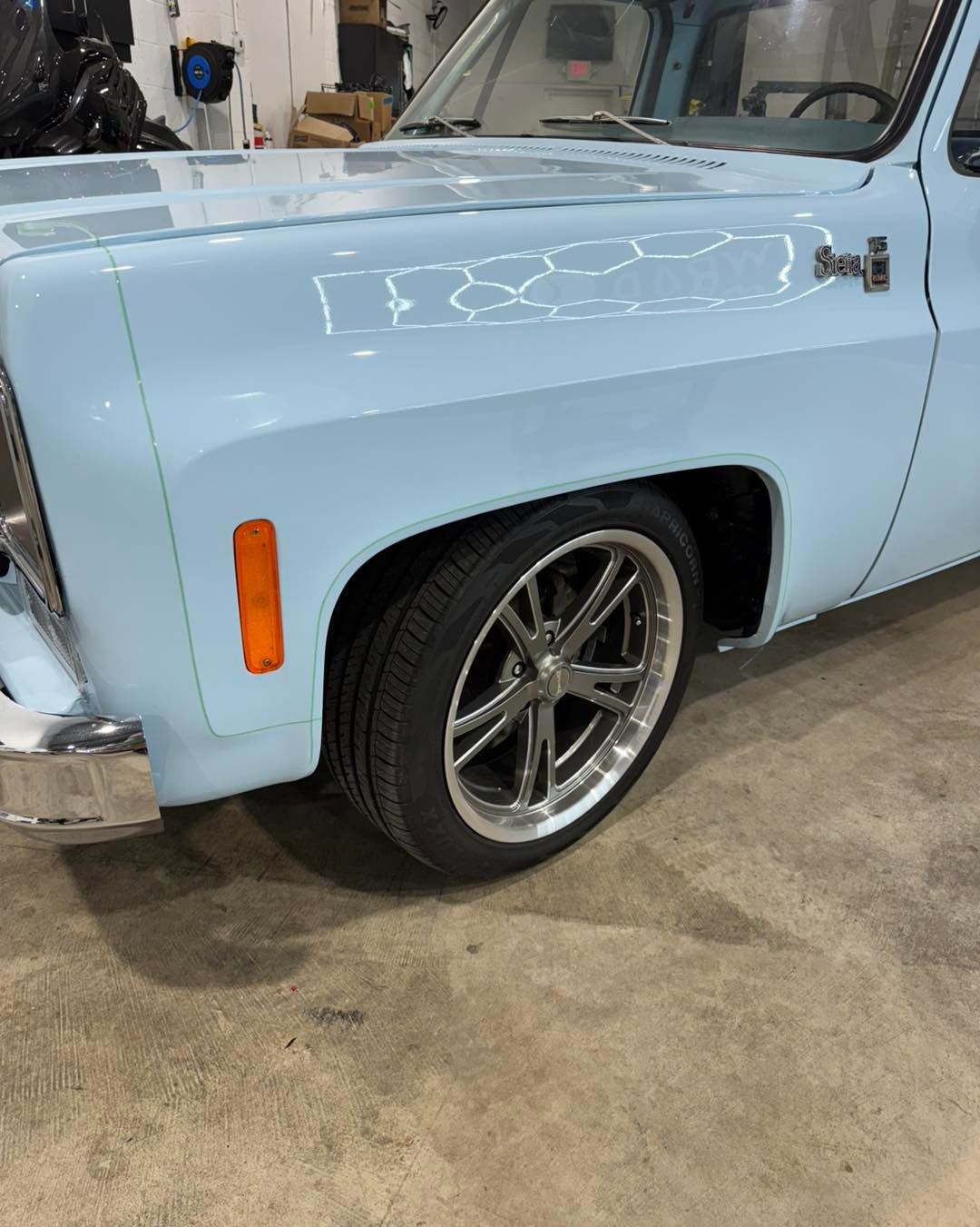 Light blue classic truck side view with chrome wheels in a garage, close-up on the front fender and tire