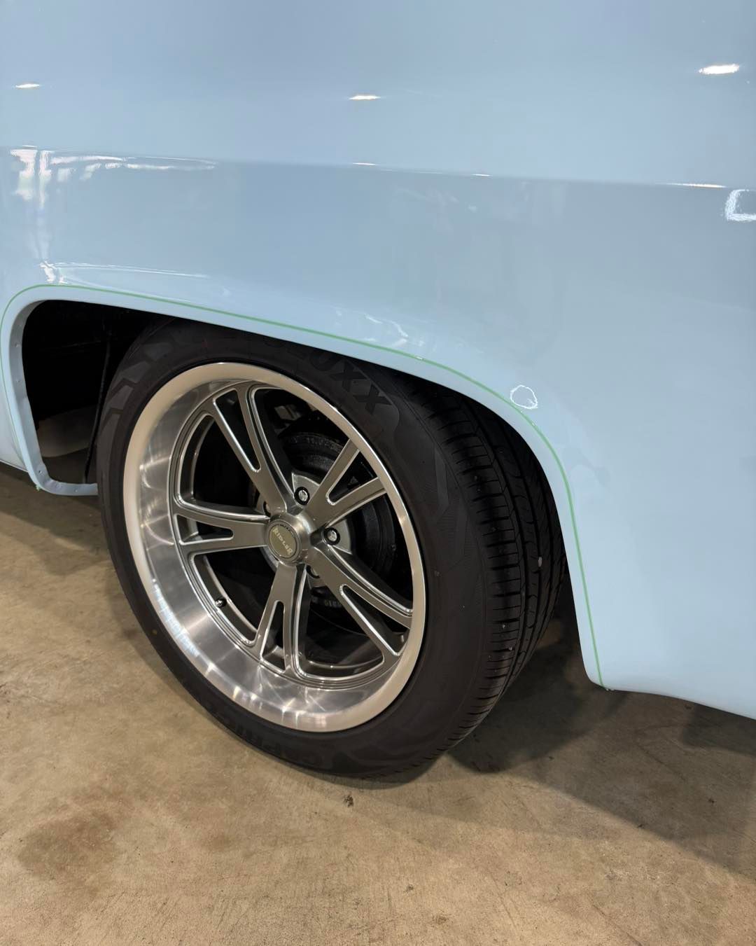 Light blue classic car rear wheel with chrome rim in a garage