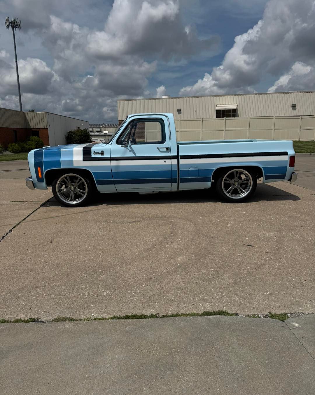 Blue and white lowered pickup truck parked on asphalt in front of a warehouse under cloudy skies