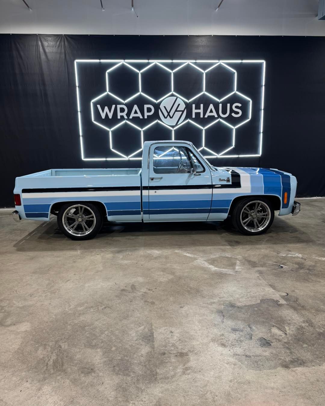 Blue classic pickup truck in a shop with a glowing Wrap Haus sign on the wall