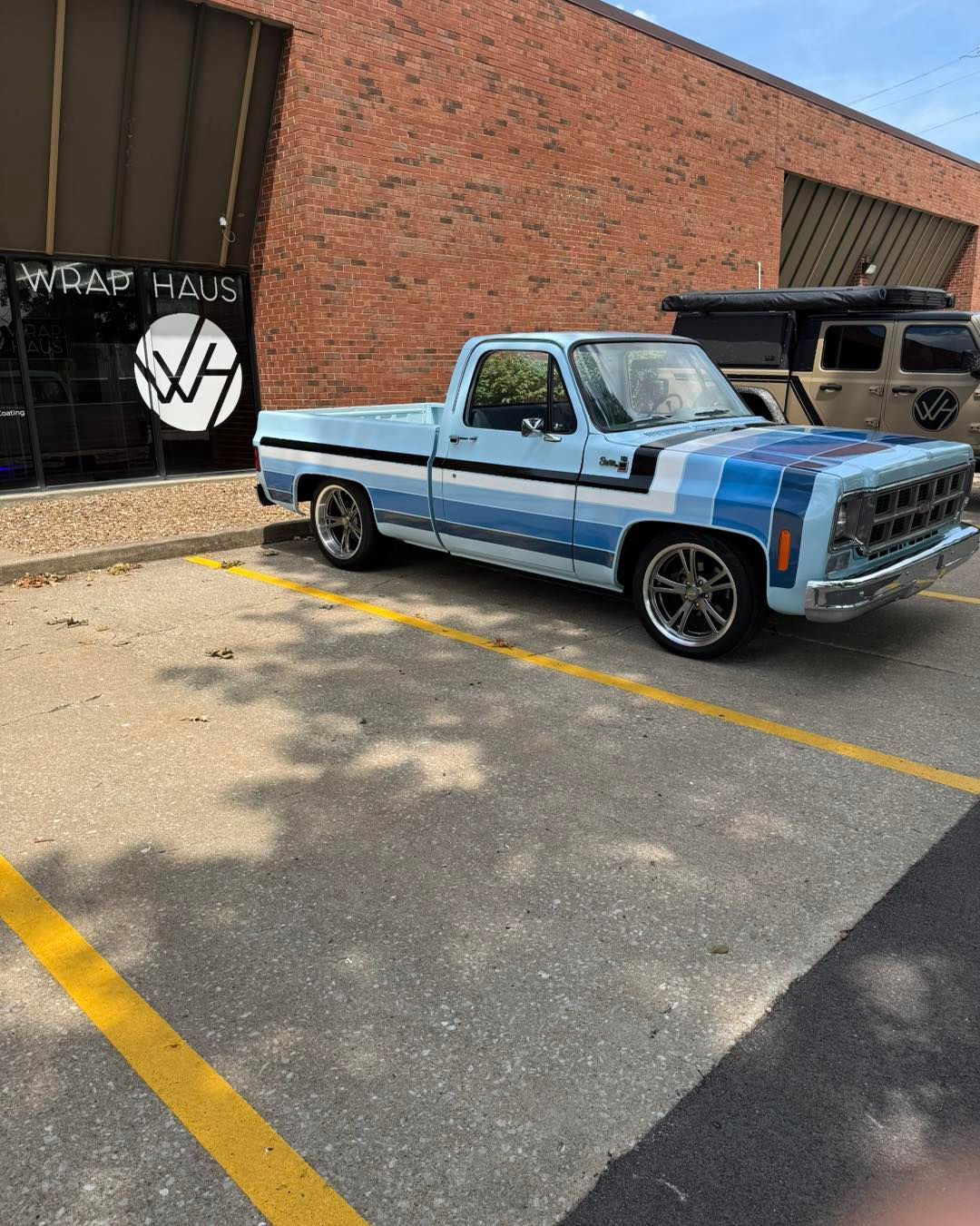 Light blue vintage pickup truck parked outside a brick building with a graffiti-covered garage door.