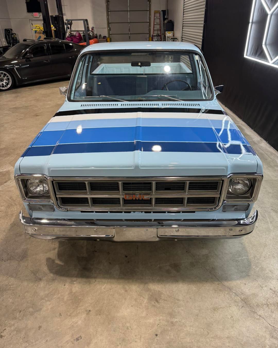 Front view of a classic white pickup with blue racing stripes parked indoors at a car show.