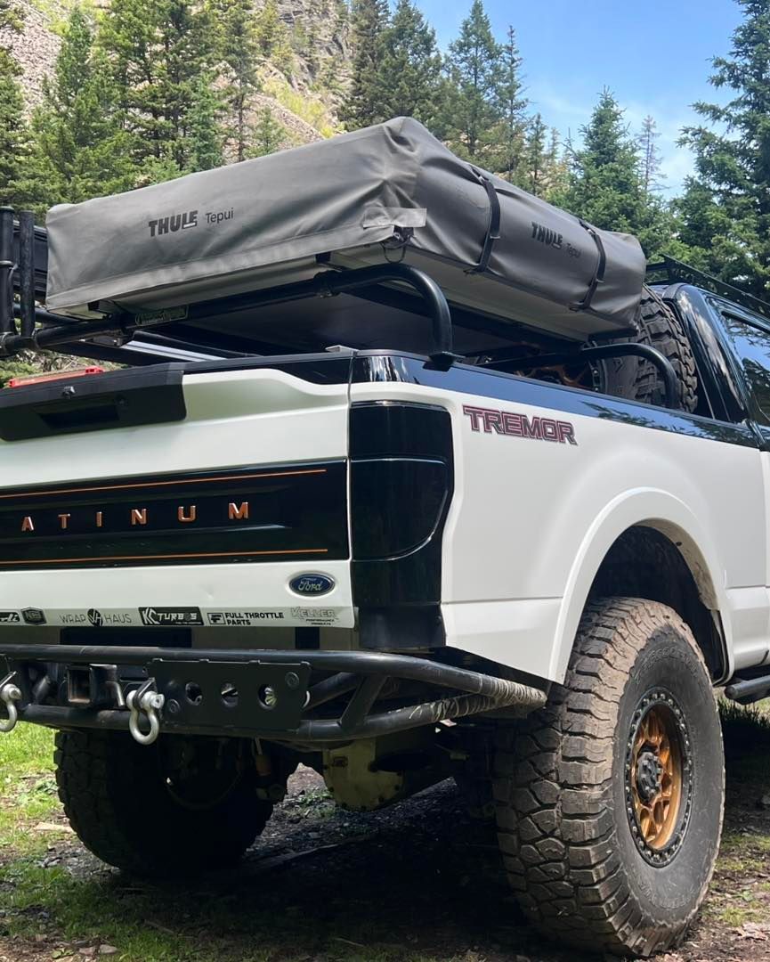 White Toyota Tundra pickup with rooftop tent parked on a dirt trail in a forest