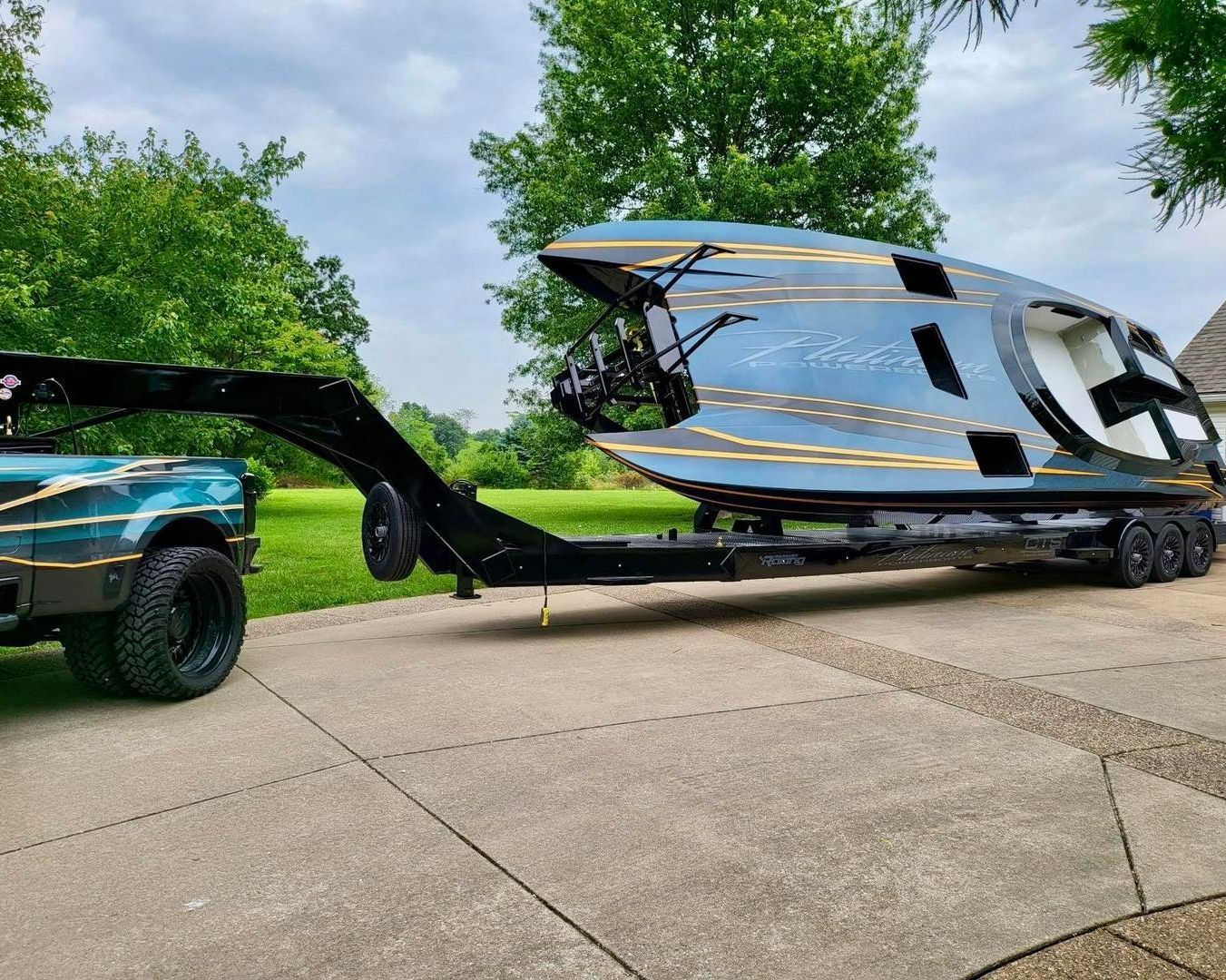 A black truck tows a shiny silver camper trailer on a driveway by green trees.
