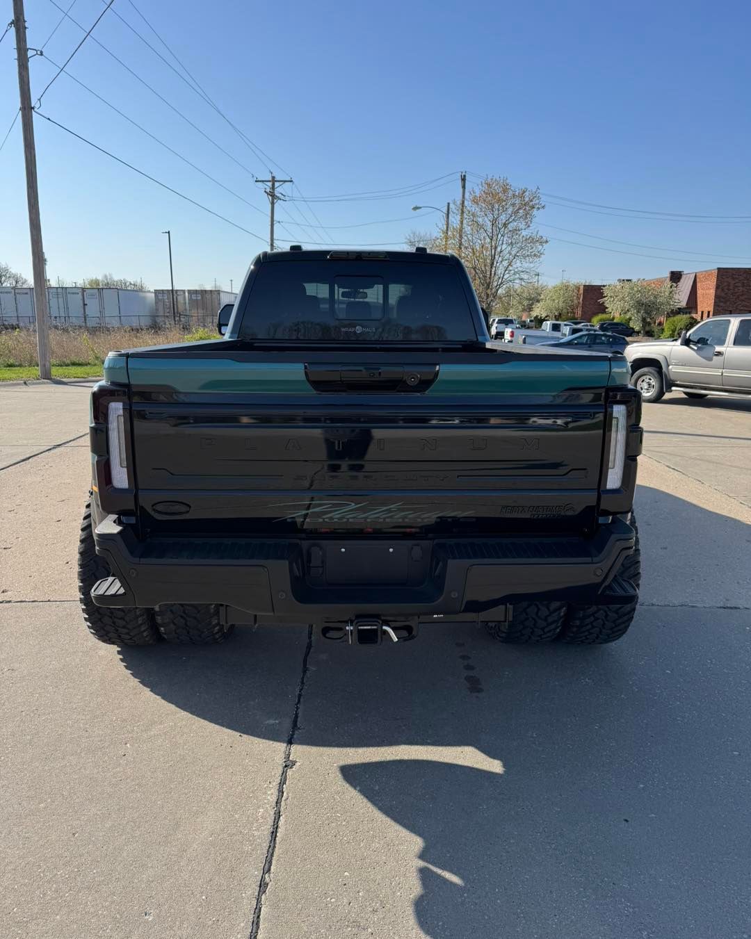 Black pickup truck seen from the rear on a sunny street, with power lines and parked cars in the background