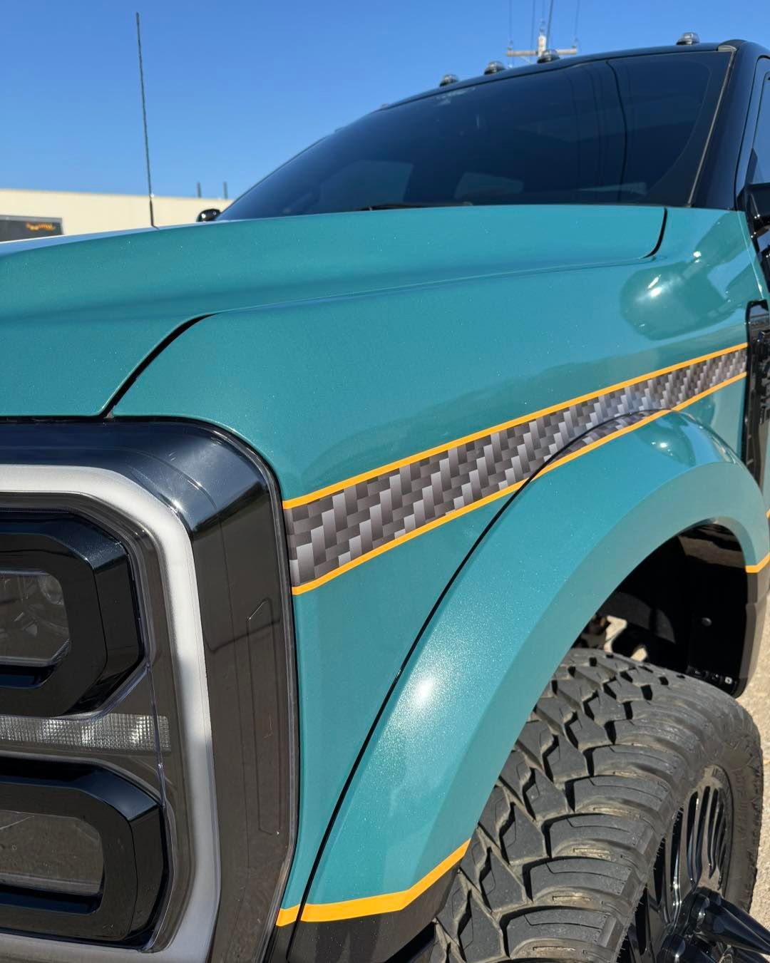 Turquoise pickup truck front fender with black grille and yellow accent stripe, close-up outdoors