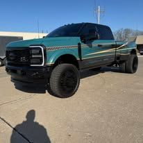 Turquoise and black lifted pickup truck parked on a sunny lot with a shadow in the foreground