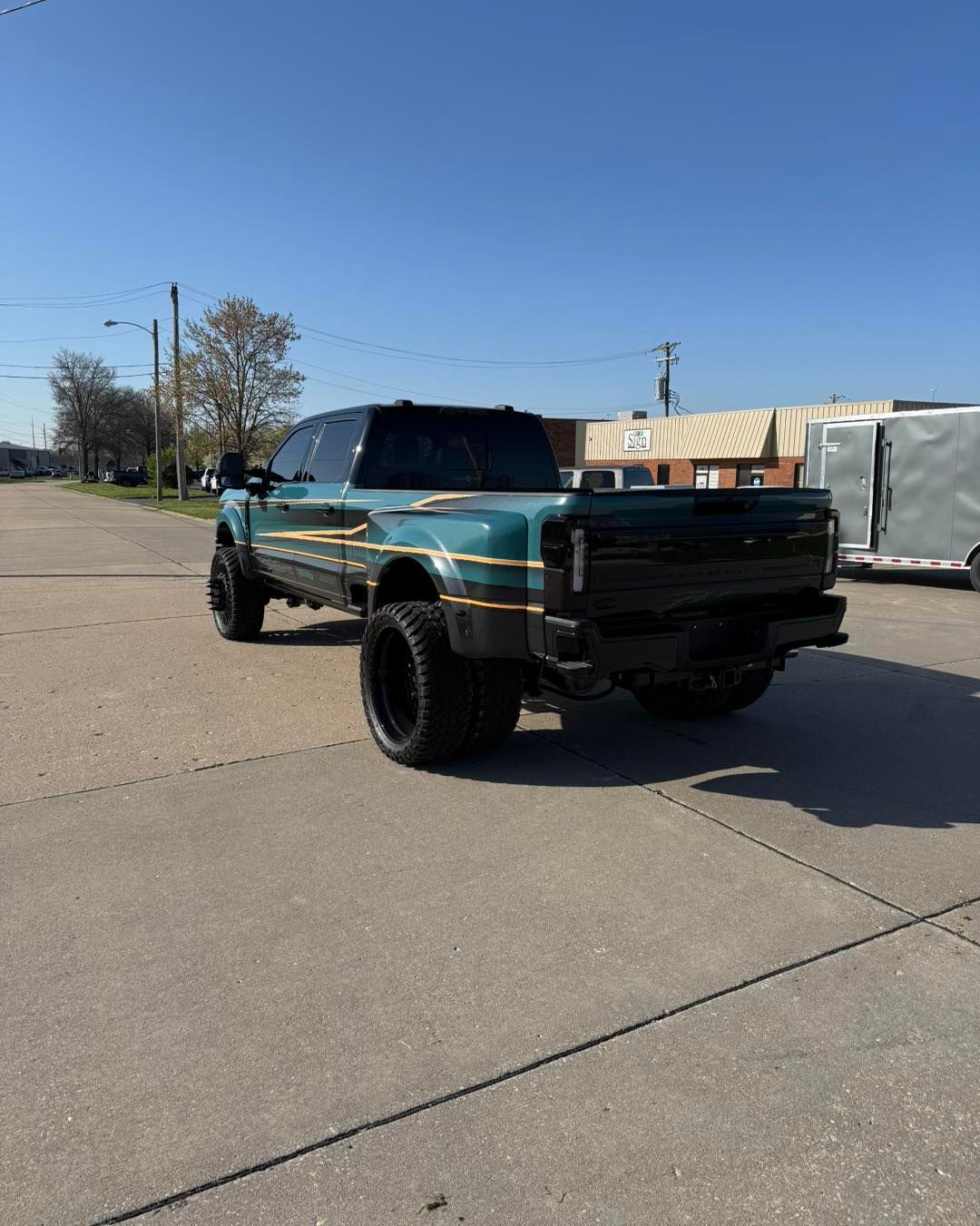 Teal-and-black lifted pickup truck parked on a sunny paved lot