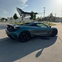 Teal sports car parked on a sunny road near a modern sculpture