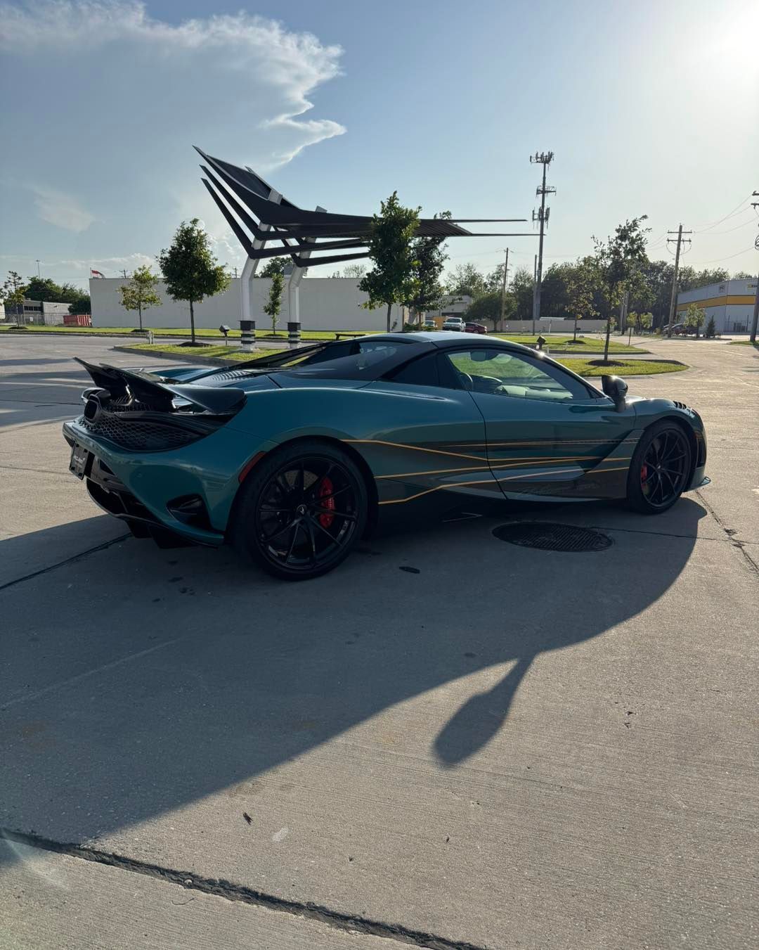 Teal sports car parked in a sunny lot near a modern sculpture