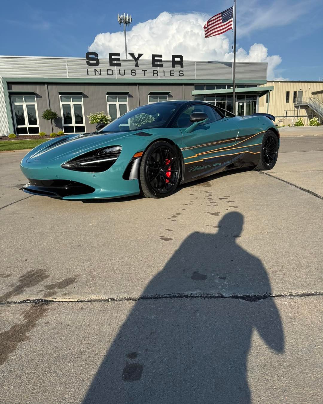 Teal sports car parked outside Beyer Industries with an American flag and shadow in the foreground
