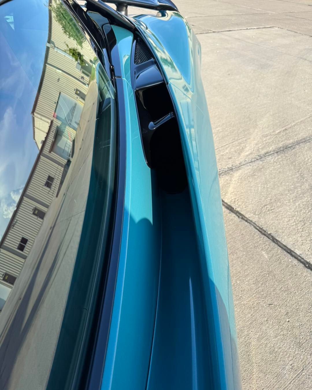 Close-up of a blue car’s hood and windshield, showing a damaged, open seam near the front edge
