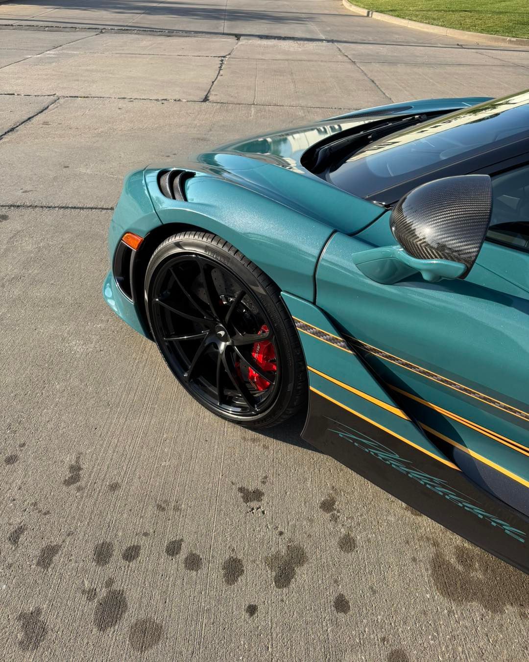 Turquoise sports car front wheel and hood on a paved street, with black rims and red brake caliper