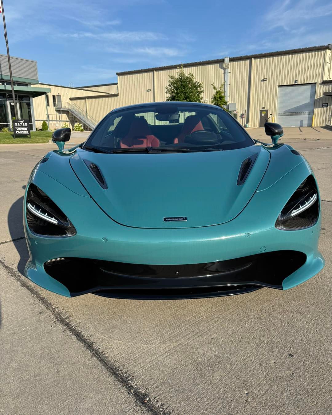 Teal sports car parked outdoors in front of an industrial building under a blue sky