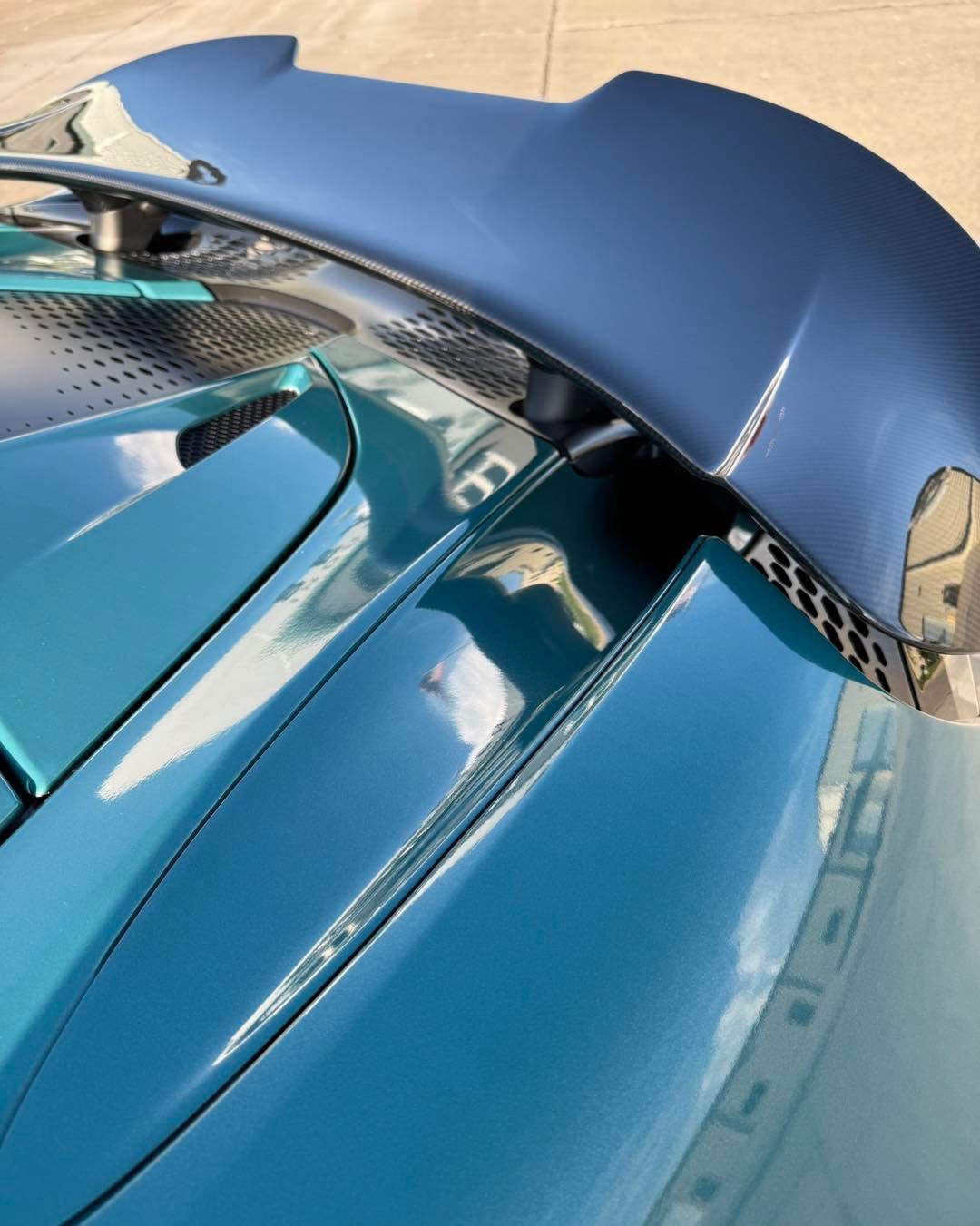 Close-up of a blue carbon-fiber sports car rear wing and glossy bodywork.