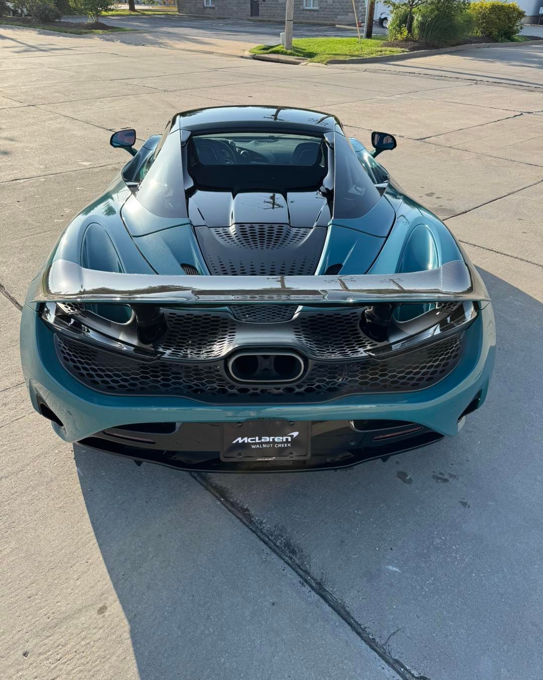 Rear view of a teal McLaren sports car parked on a concrete street in daylight