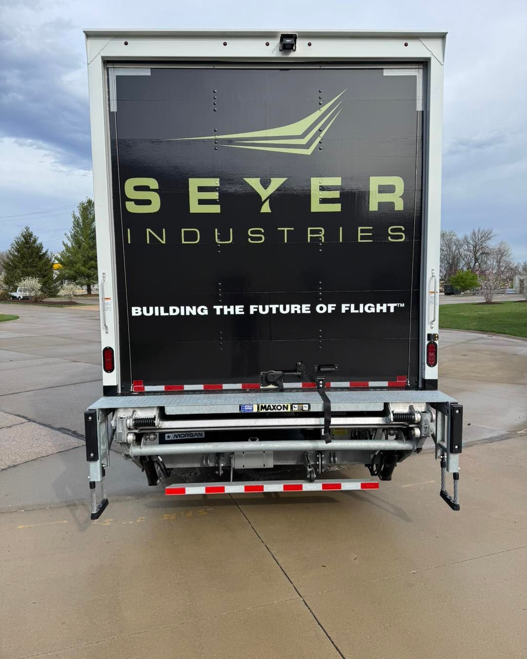 Rear of a Seyer Industries truck with logo and slogan, parked on a wet road.