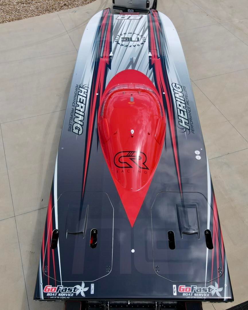Red and black racing boat viewed from above on pavement, with a glossy hull and central cockpit cover