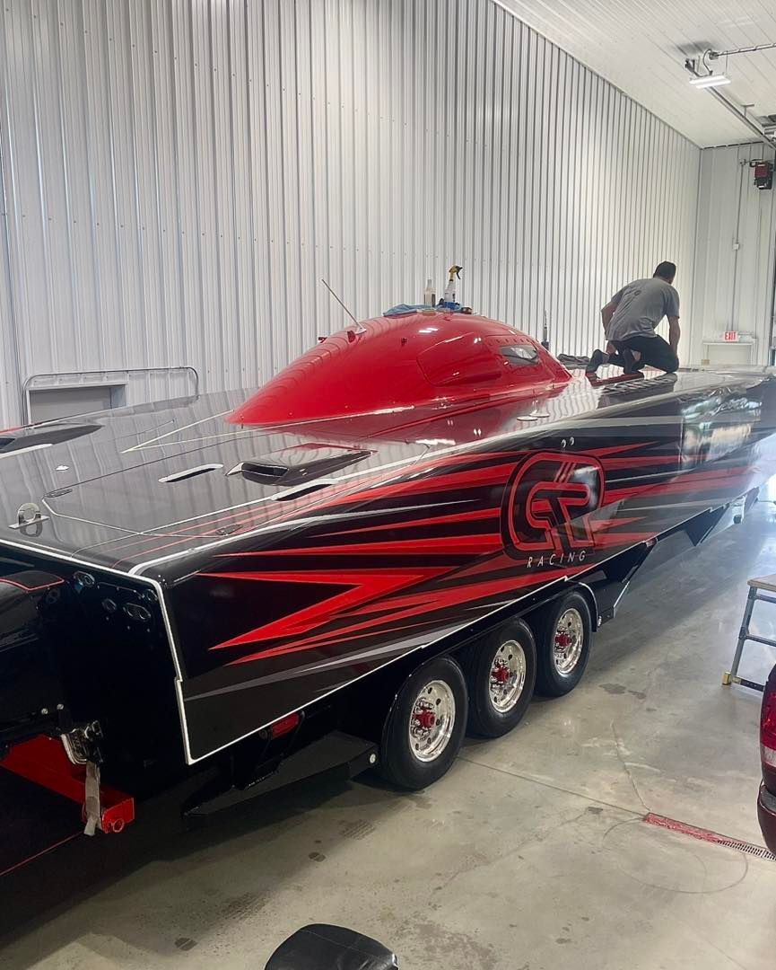 Red and black custom race trailer with chrome details inside a garage, with a person standing beside it.