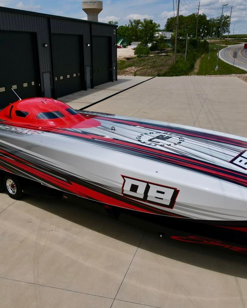 Red and white speedboat with number 09 parked on a concrete lot near a building