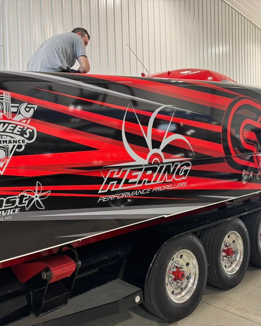 Red and black racing speedboat on a trailer, with a person leaning over the top inside a covered area.
