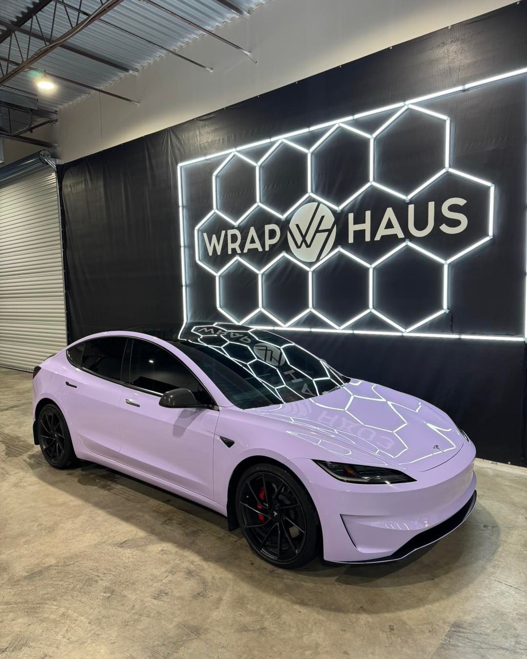 Lavender sports car parked inside a Wrap Haus shop with a glowing hexagon wall sign.