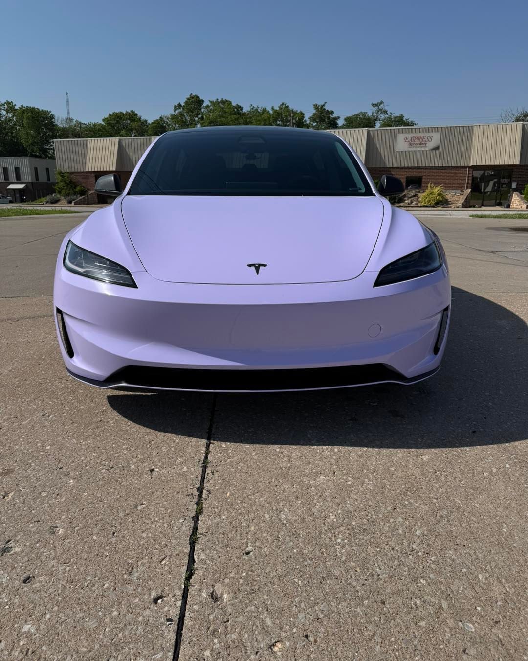 Light purple Tesla sedan parked on an asphalt lot under a clear blue sky
