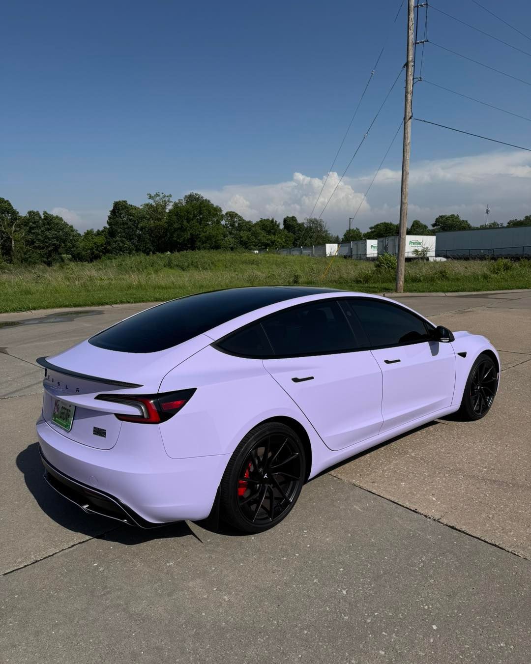 Light purple sedan with black wheels parked on a concrete lot under a clear blue sky.