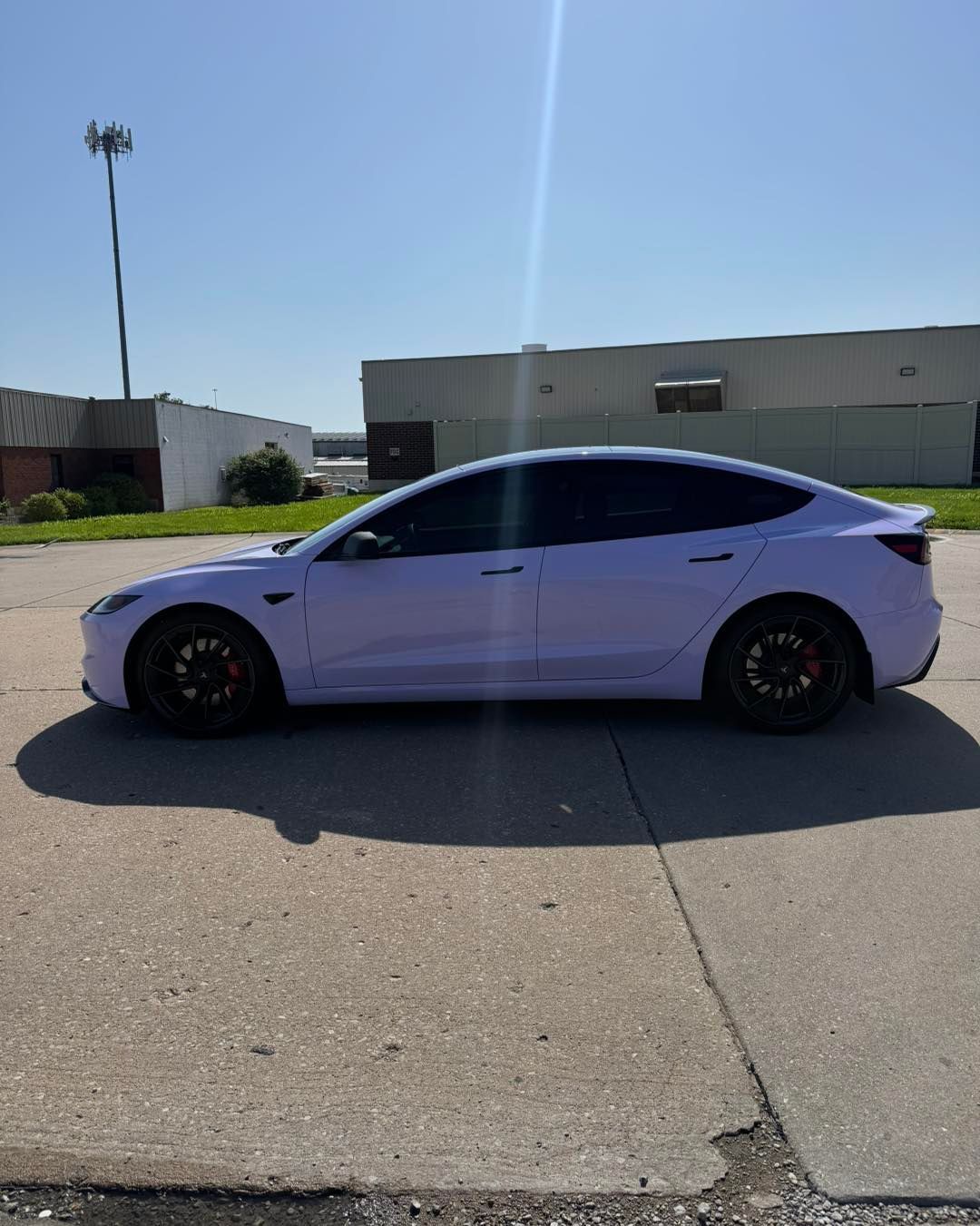Lavender sedan parked on a sunlit street beside industrial buildings