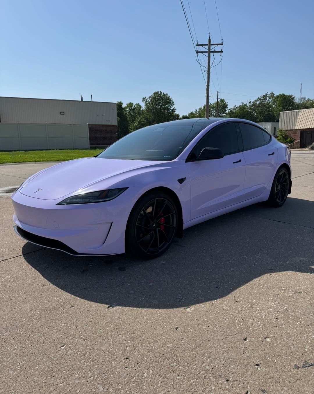 Lavender Tesla sedan parked on a sunny street beside a building and utility poles