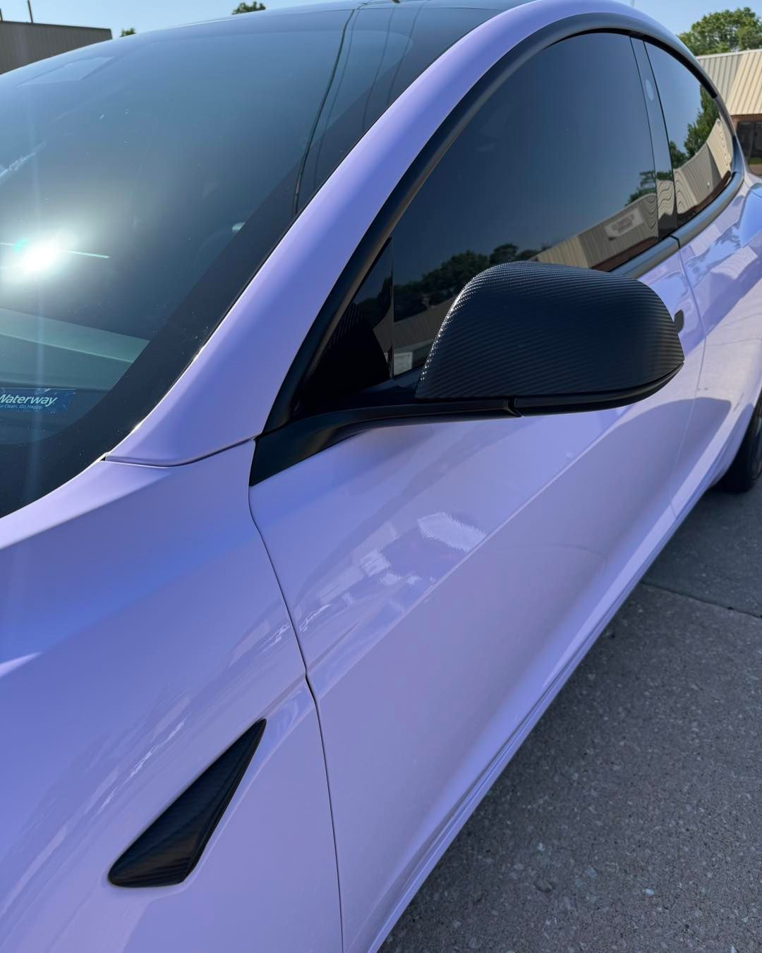Close-up of a lavender car’s side mirror and tinted window in a parking lot