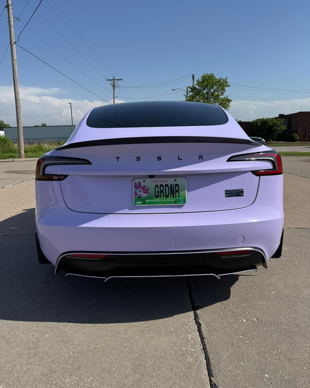 Rear view of a white Tesla sedan with a green license plate parked on a sunny street.