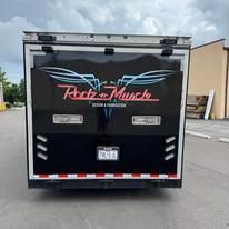 Black trailer with pink “Robz Muscle” logo parked in an industrial lot, rear view.