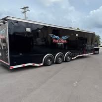 Black enclosed trailer with “Patsy” logo parked on a lot under cloudy skies