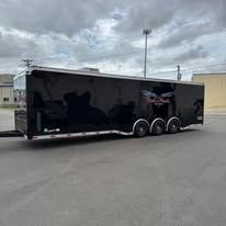 Black enclosed car hauler trailer parked in a lot under a cloudy sky