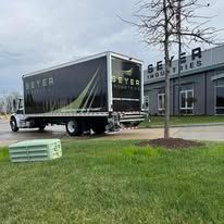 Gray delivery truck outside a Beyer office building, with pallets on the grass in front.